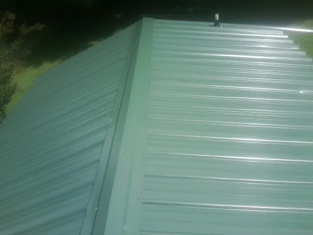 New green metal panels meeting at the ridge of a roof — Flat Roof Repair work by our crew in Trenton
