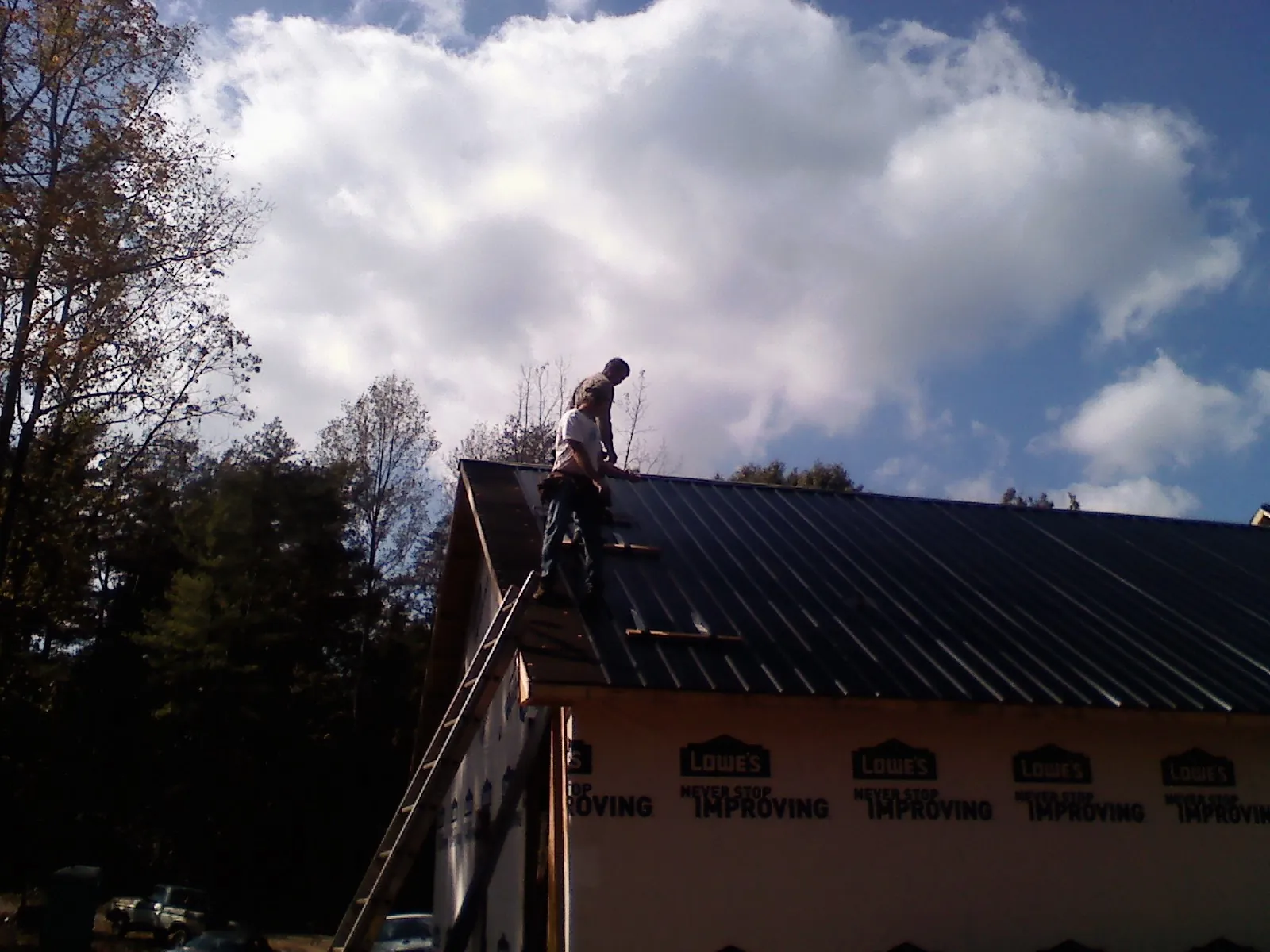 Roofer fastening dark metal panels high against a cloudy sky, from a Roof Inspection job in Trenton